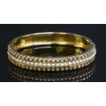 A late Victorian gold, split pearl and coral hinged bangle,with a central row of split pearls, all
