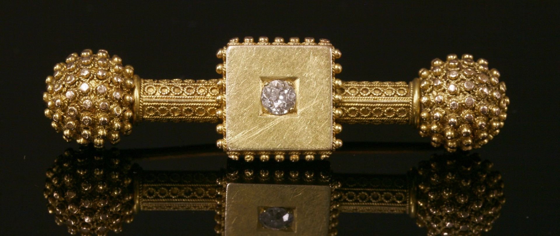 A Victorian gold Etruscan Revival, single stone, diamond dumb-bell bar brooch, c.1870,with a plain