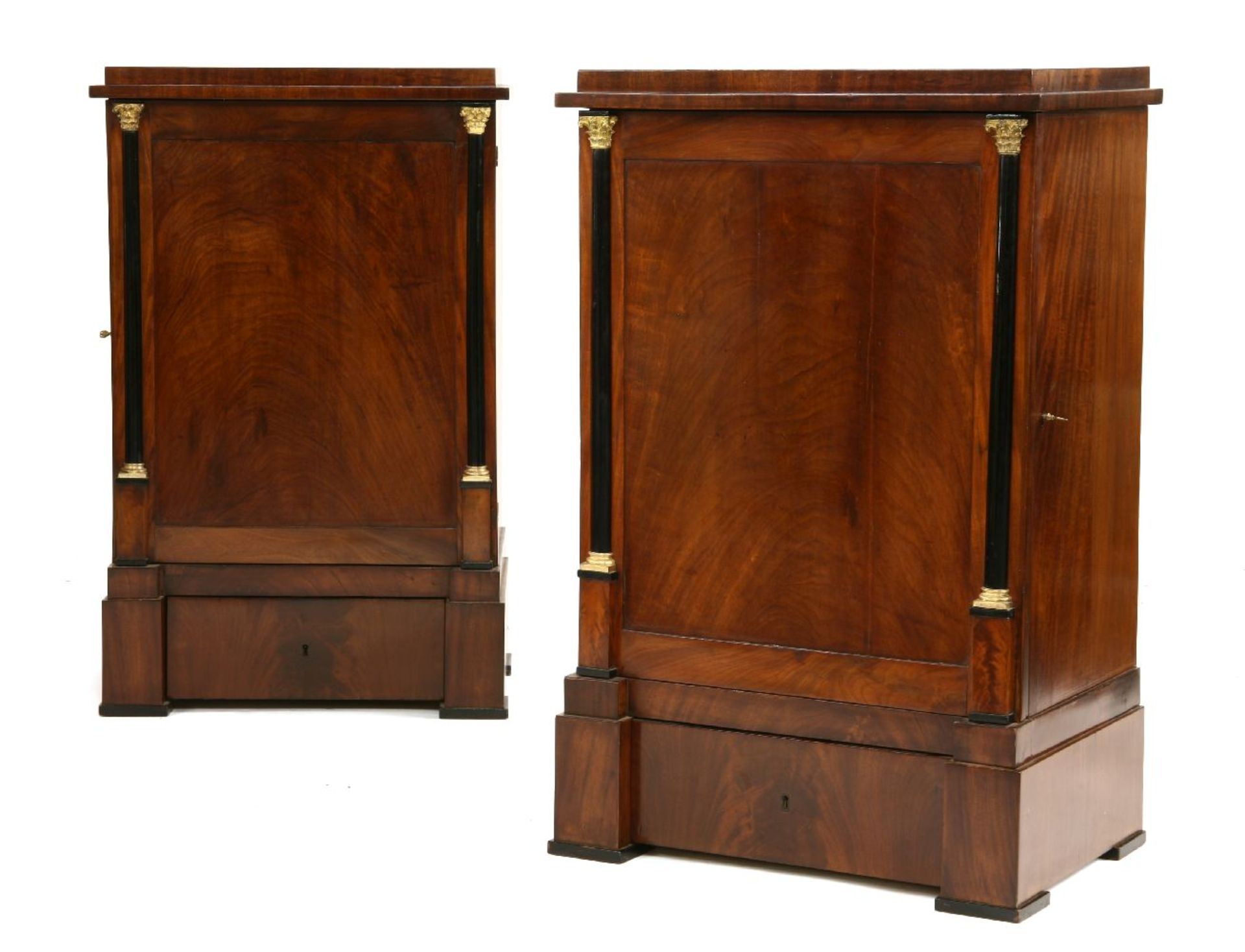 A pair of Biedermeier pedestal cabinets,the stepped tops over doors with brass-capped ebony half