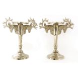 A pair of silvered candle stands, each with stag's head handles to either side, and on a faceted