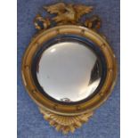 A Regency style circular convex wall hanging looking glass surmounted with an open winged eagle,