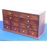 A tabletop bank of eleven varying sized mahogany drawers,
