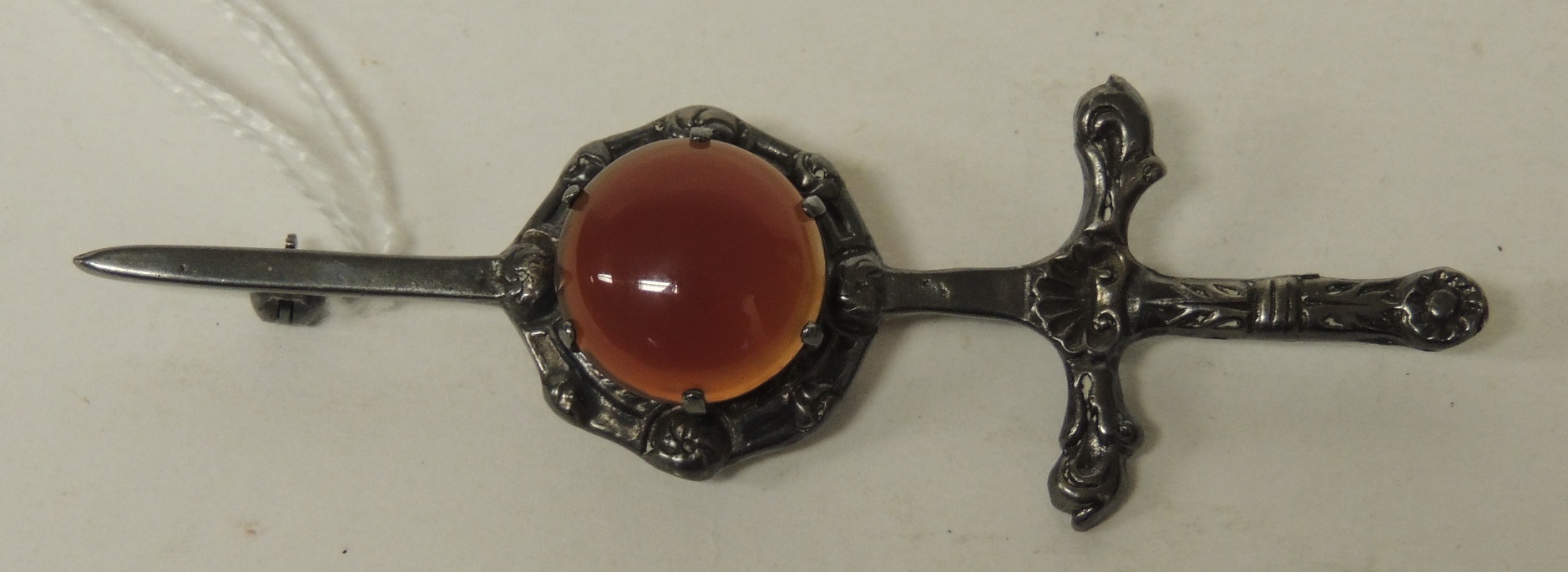 A Scottish silver brooch in the form of a sword and circular shield with a cabochon carnelian,