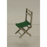 A 20th Century miniature silver chair modelled as a folding chair with green felt seat, 4.5cms high,