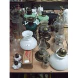 A turquoise glass oil lamp base together with a collection of other oil lamps and shades.
