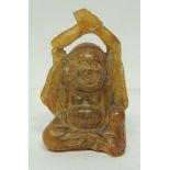 A 19th Century Chinese amber netsuke carved in the figure of Hotei with arms raised, 6cms high