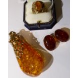 A 9 carat gold amber pendant, a large amber drop to an abstract scroll and beaded bail, measures 9cm