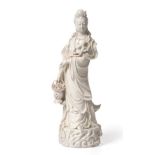 A Blanc de Chine Figure of Guanyin, 18th/19th century, standing holding a flower and a basket of
