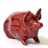 A Wemyss Pottery Figure of a Small Pig, early 20th century, decorated with a ruby coloured glaze,