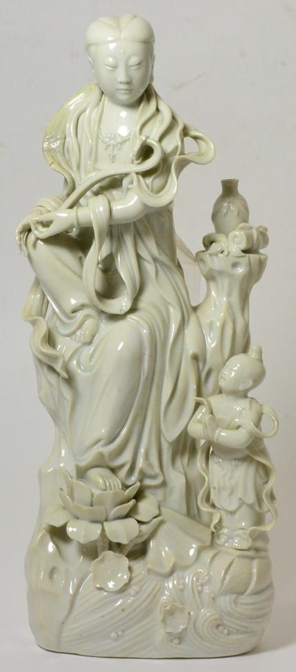 A Chinese Blanc de Chine Figure of Guanyin, Qing Dynasty, sitting on a rocky outcrop, an attendant