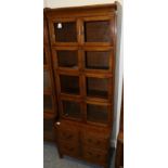 A 1920s Oak Bookcase, with eight glazed doors, the base with four deep drawers, raised on turned