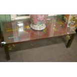A Chinese lacquered coffee table with brass legs and a glass top