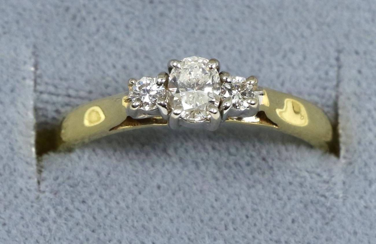 An 18 carat gold diamond three stone ring, an oval cut diamond between two round brilliant cut