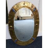 An Arts & Crafts Brass Wall Mirror, circa 1910, of oval form with bevelled plate, the hammered frame