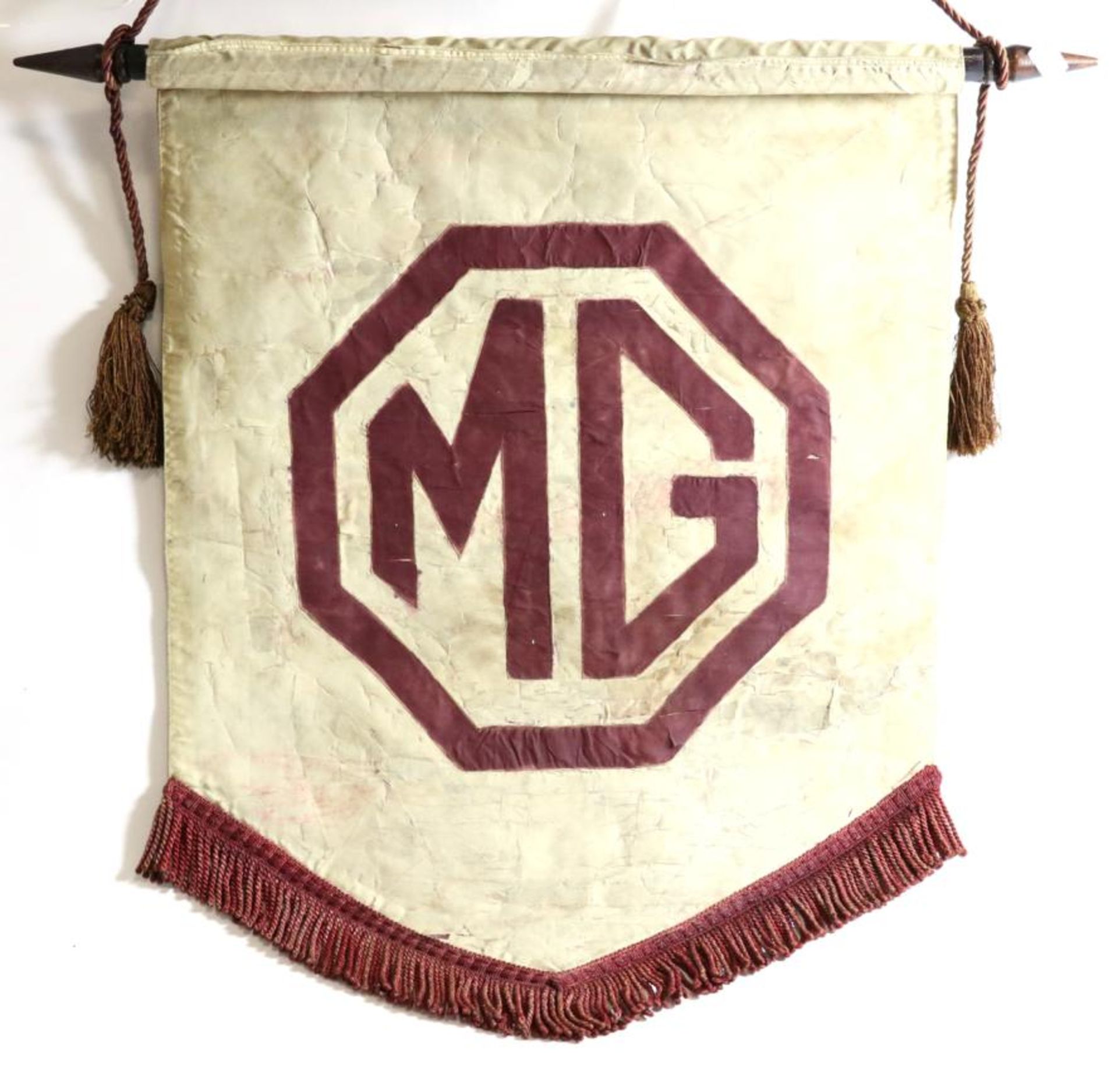 A Vintage MG Pennant Flag on Fabric, of shield shaped form with tasselled edge, suspended on a