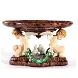 A Minton Majolica Centrepiece, 1870, the lobed oval bowl supported by two putti flanking a pair of