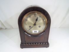 An oak cased mantel clock, Arabic numerals on a silvered dial,