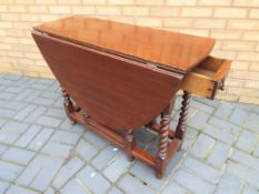 An oak gate-leg table with single drawer raised on barley twist supports,