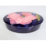 Moorcroft Pottery - a lidded oval trinket dish decorated with pink magnolia on a blue ground,