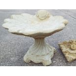 A large stone bird bath with a shell decoration,