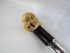 A walking stick with a bone carved skull and a white metal collar.