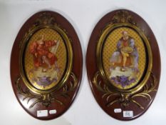 Two ceramic wall plaques decorated with images of artists with brass surrounds mounted on oval