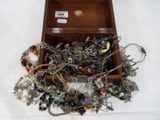 A wooden jewellery box containing a quantity of predominantly white metal costume jewellery - This