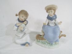 Two Nao figurines, the first depicting a young girl with a doll,