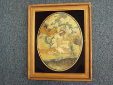 A Regency printed silk and needlework oval picture depicting a woman dressed in finery seated by a
