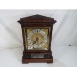 A carved oak cased mantel clock Roman numerals on a silvered dial,