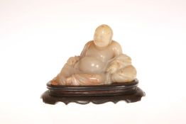 A SOAPSTONE FIGURE OF A RECLINING BUDDHA, 19th CENTURY, mounted on a hardwood stand.