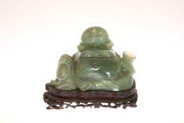 A CARVED JADE FIGURE OF A SEATED BUDDHA, modelled with a cup in his left hand, on a hardwood stand.