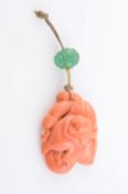 A CHINESE CARVED CORAL PLAQUE, suspending on fabric cord with carved green bead. Weight 13.5 grams.