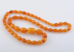 AN AMBER BEAD NECKLACE, formed of fifty-one graduating oval amber beads.