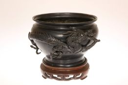 A JAPANESE BRONZE BOWL, MEIJI PERIOD, with encircling dragon in high relief, on a wooden stand.