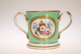 A STAFFORDSHIRE GREEN GROUND LOVING CUP, 19TH CENTURY, painted with flowers within a gilt cartouche,