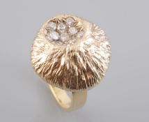 A DIAMOND AND GOLD RING, the unusual domed circular mount of textured metal detailing,
