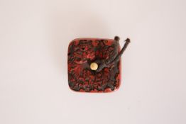 A JAPANESE RED LACQUER MANJU NETSUKE, 19th Century, of cushioned square shape with ivory peg.