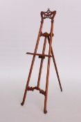 AN ART NOUVEAU CARVED MAHOGANY EASEL, the crest carved as whiplash and stylised foliage.