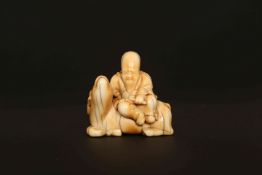 A JAPANESE IVORY NETSUKE, PROBABLY LATE 18th/EARLY 19th CENTURY, of a bearded sage seated on a deer.