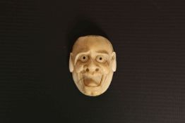 A JAPANESE IVORY MASK NETSUKE, MEIJI PERIOD, of a man with staring eyes and gaping mouth.