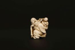 A JAPANESE IVORY NETSUKE, MEIJI PERIOD, of a crouching sage, a child pulling his beard.