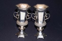 Pair of silver two handled vases of hexagonal form with ornate band and stepped base, London 1927,