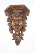 A 19TH CENTURY CARVED WALNUT WALL BRACKET, carved as Bacchus draped in fruiting vine.