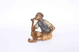 A COLD PAINTED BRONZE OF A BOY SMOKING A PIPE, modelled seated with crossed legs,