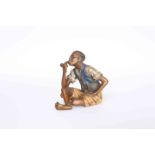 A COLD PAINTED BRONZE OF A BOY SMOKING A PIPE, modelled seated with crossed legs,