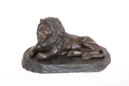 A BRONZE OF A RECLINING LION, on a wooden stand.