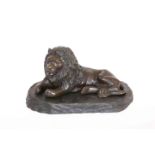 A BRONZE OF A RECLINING LION, on a wooden stand.