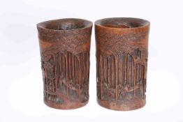 A PAIR OF CHINESE BAMBOO BRUSH POTS, CIRCA 1900, carved with figures in a wooden landscape. 21.