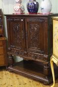 Caved oak cabinet having two carved doors above two carved drawers with undershelf below,